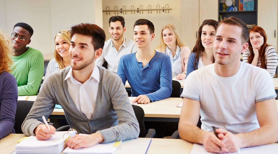 Eine Gruppe junger Erwachsener sitzt in einem Klassenraum, hört aufmerksam zu und macht sich Notizen. Sie wirken motiviert und konzentriert. Eine Gruppe junger Erwachsener sitzt in einem Klassenraum, hört aufmerksam zu und macht sich Notizen. Sie wirken motiviert und konzentriert.