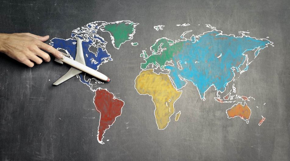Schule International Hand mit Flugzeug überfliegt eine Weltkarte auf eine Tafel mit Kreide, umgeben von Notizen und Skizzen.