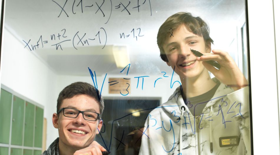 Zwei Jungs beschreiben eine Glasscheibe mit mathematischen Formeln. Zwei Jungs beschreiben eine Glasscheibe mit mathematischen Formeln.
