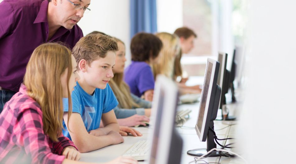Ein Mann und mehrere Kinder sitzen vor Computern und arbeiten gemeinsam an einem Projekt. Ein Mann und mehrere Kinder sitzen vor Computern und arbeiten gemeinsam an einem Projekt.