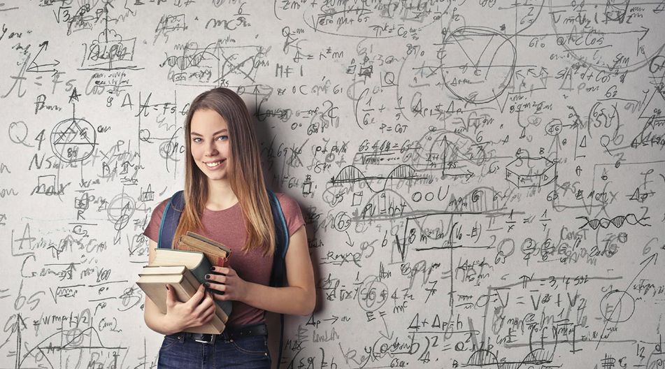 Eine junge Frau mit langen braunen Haaren steht lächelnd vor einer Wand voller mathematischer Formeln und Skizzen. Sie hält mehrere Bücher in den Armen und trägt einen Rucksack. Eine junge Frau mit langen braunen Haaren steht lächelnd vor einer Wand voller mathematischer Formeln und Skizzen. Sie hält mehrere Bücher in den Armen und trägt einen Rucksack.